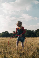 Girl playing with hoop at grass area in park - ASGF01724