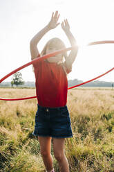 Mädchen spinnt Hula-Hoop-Reifen beim Spielen im Park an einem sonnigen Tag - ASGF01731