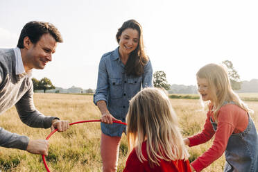 Lächelnde Familie spielt mit Hula-Hoop-Reifen im Park am Wochenende - ASGF01735