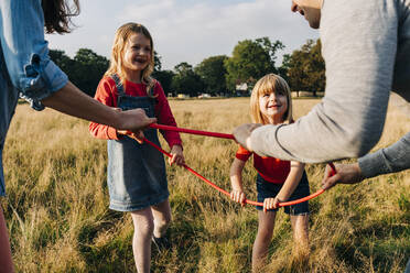 Daughters and parents holding hula hoop while playing in park - ASGF01736