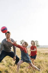 Glückliche Geschwister und Vater spielen mit Ball im Park - ASGF01749