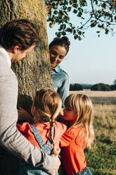 Familie umarmt Baum im Park an einem sonnigen Tag - ASGF01758