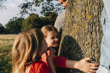 Girl hugging tree by parents and sister in park - ASGF01759