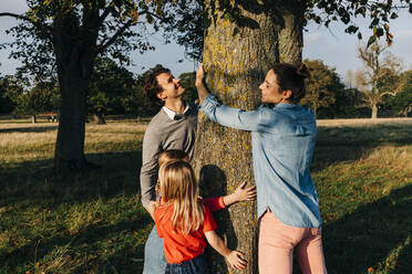 Eltern und Töchter umarmen am Wochenende einen Baum im Park - ASGF01760