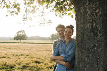 Couple standing by tree in park on sunny day - ASGF01767