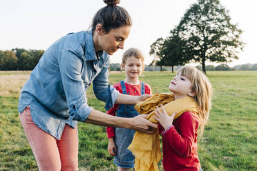 Mother putting scarf around daughter's neck in park - ASGF01778