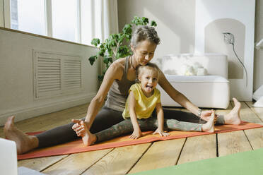 Mother helping daughter doing legs split on exercise mat - SEAF00115