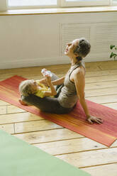 Cheerful mother sitting with daughter on exercise mat - SEAF00123