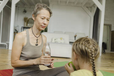 Mother looking at daughter eating fruit at home - SEAF00129