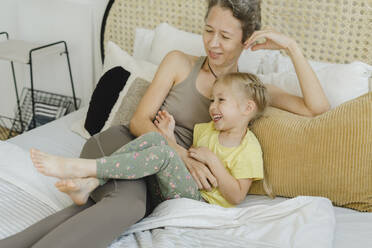 Happy daughter resting with mother on bed at home - SEAF00130