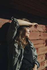 Smiling woman shielding eyes and leaning on wall - SEAF00135