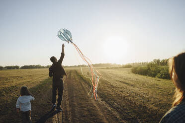 Playful family playing with kite on dirt road - SEAF00153