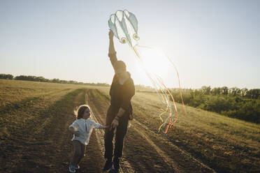 Daughter playing with father holding kite on dirt road - SEAF00154