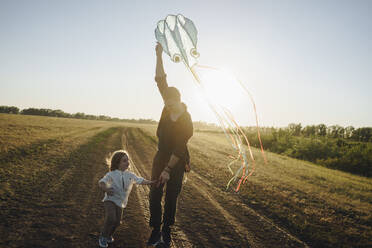 Tochter spielt mit Vater, der einen Drachen auf einem Feldweg hält - SEAF00154