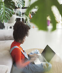 Curly haired woman using laptop at home - JCCMF04584