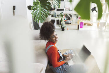 Smiling young woman with laptop in living room - JCCMF04585