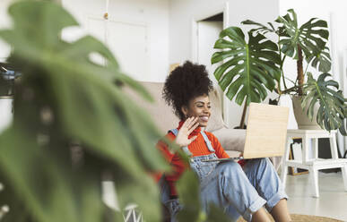 Smiling woman waving during video call through laptop at home - JCCMF04586