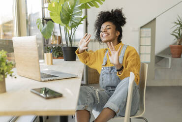 Smiling woman greeting on video call through laptop at table - JCCMF04607