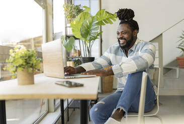 Hipster man laughing and using laptop at home - JCCMF04609