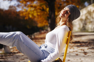 Smiling teenage girl with eyes closed relaxing on chair - DAWF02298