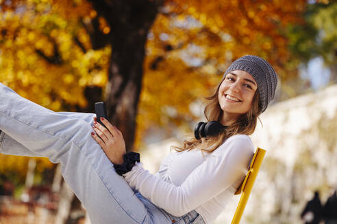 Smiling teenage girl with smart phone sitting in public park - DAWF02304