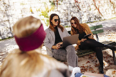 Smiling businesswoman sharing laptop with colleague on bench - DAWF02310