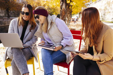 Happy businesswoman with laptop discussing with colleague on sunny day - DAWF02313