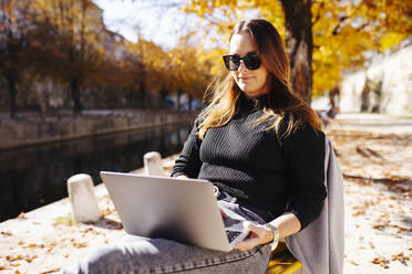 Junge Geschäftsfrau mit Sonnenbrille und Laptop an einem sonnigen Tag - DAWF02318
