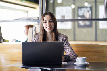 Smiling businesswoman using laptop at cafe table - IFRF01248