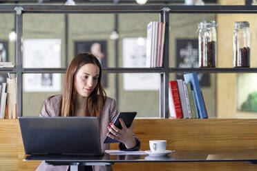 Junge Geschäftsfrau mit Laptop und Smartphone in einem Café - IFRF01249