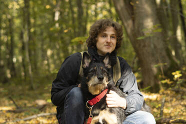 Smiling man with dog sitting in forest - SSGF00266