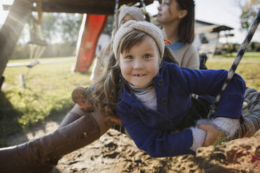 Mädchen schaukelt mit Familie auf einer Schaukel auf dem Spielplatz - LLUF00367