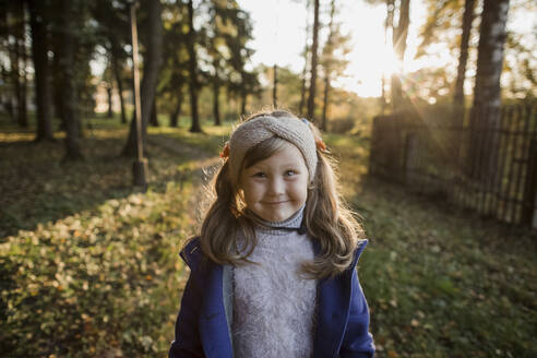 Smiling girl standing on grass at sunset - LLUF00370