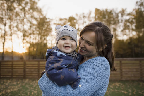 Mother carrying cheerful baby boy at lawn - LLUF00374