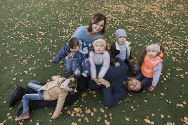 Family sitting together on lawn covered with autumn leaves - LLUF00375