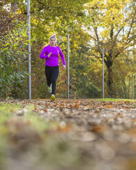Weiblicher Teenager joggt auf gefallenen Herbstblättern - STSF03118