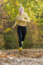 Weiblicher Teenager joggt auf gefallenen Herbstblättern - STSF03119