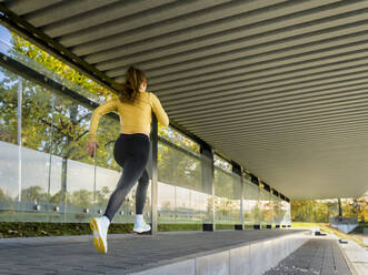 Weiblicher Teenager joggt unter dem Vordach eines Gebäudes - STSF03120