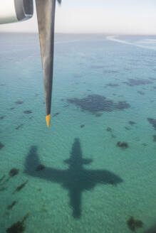 Der Schatten eines Flugzeugs spiegelt sich auf türkisfarbenem Wasser, - CAVF95257