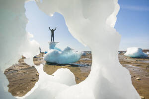 Mann steht mit erhobenen Armen auf der Spitze eines Eisbergs, Baffin Island. - CAVF95264