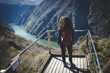 Frau mit rotem Rucksack und lockigem Haar, die die Landschaft von oben betrachtet - CAVF95279