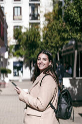 Businesswoman with backpack and mobile phone at city street - EBBF04815