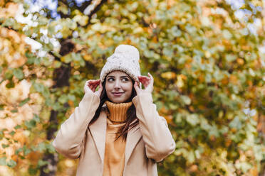 Smiling woman wearing knit hat in autumn park - EBBF04825