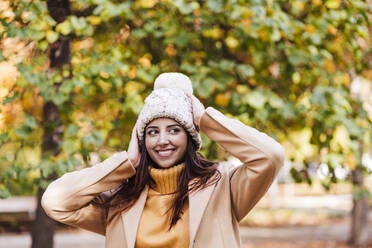 Smiling young woman with knit hat at autumn park - EBBF04827