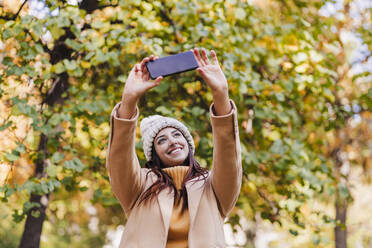 Lächelnde Frau nimmt Selfie durch Smartphone im Park - EBBF04829