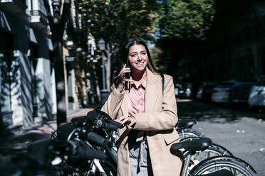 Businesswoman talking on mobile phone at bicycle parking station - EBBF04839