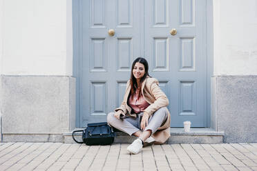 Smiling businesswoman sitting with backpack on doorstep - EBBF04843