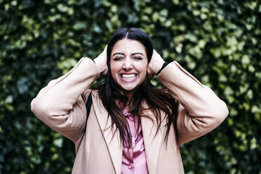 Smiling businesswoman covering ears in front ivy plants - EBBF04852