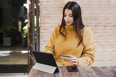 Woman with credit card using digital tablet at sidewalk cafe - EBBF04854