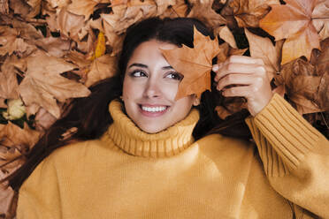 Smiling woman holding dry maple leaf - EBBF04863